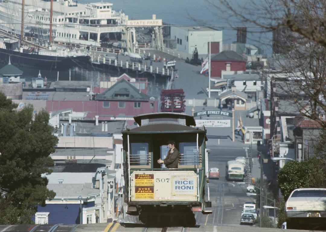 A Hyde Street cable car makes its way up Russian Hill in San Francisco, California, on June 21st, 1974. In the background is San Francisco Bay.