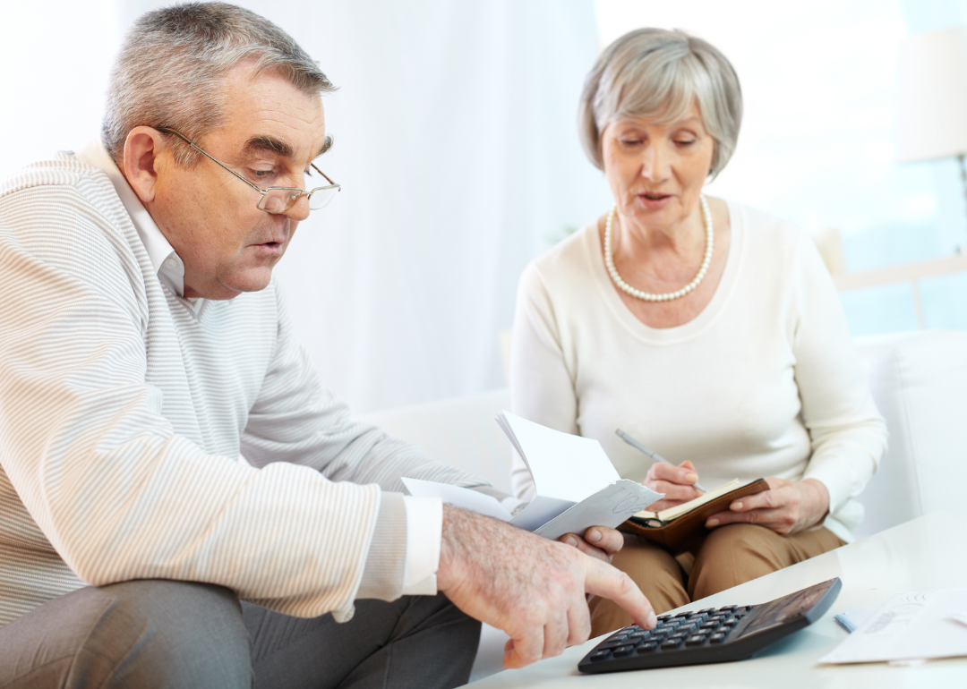 A senior couple sit on a couch with calculator budgeting.