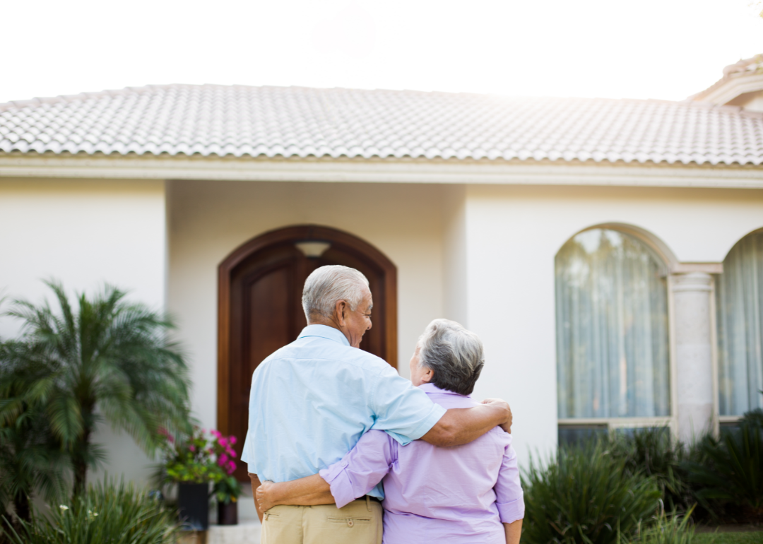 Retired couple embrace while looking at their Spanish-style home.