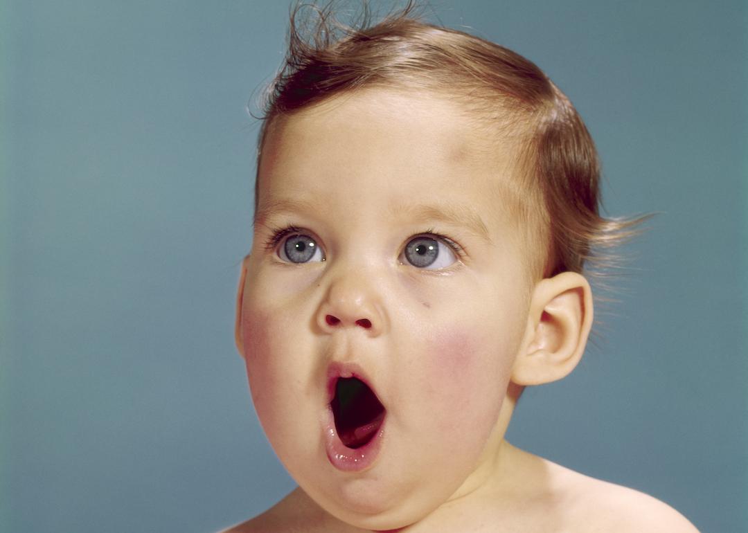 Surprised baby with brown hair and blue eyes with their mouth open in the 1960s.