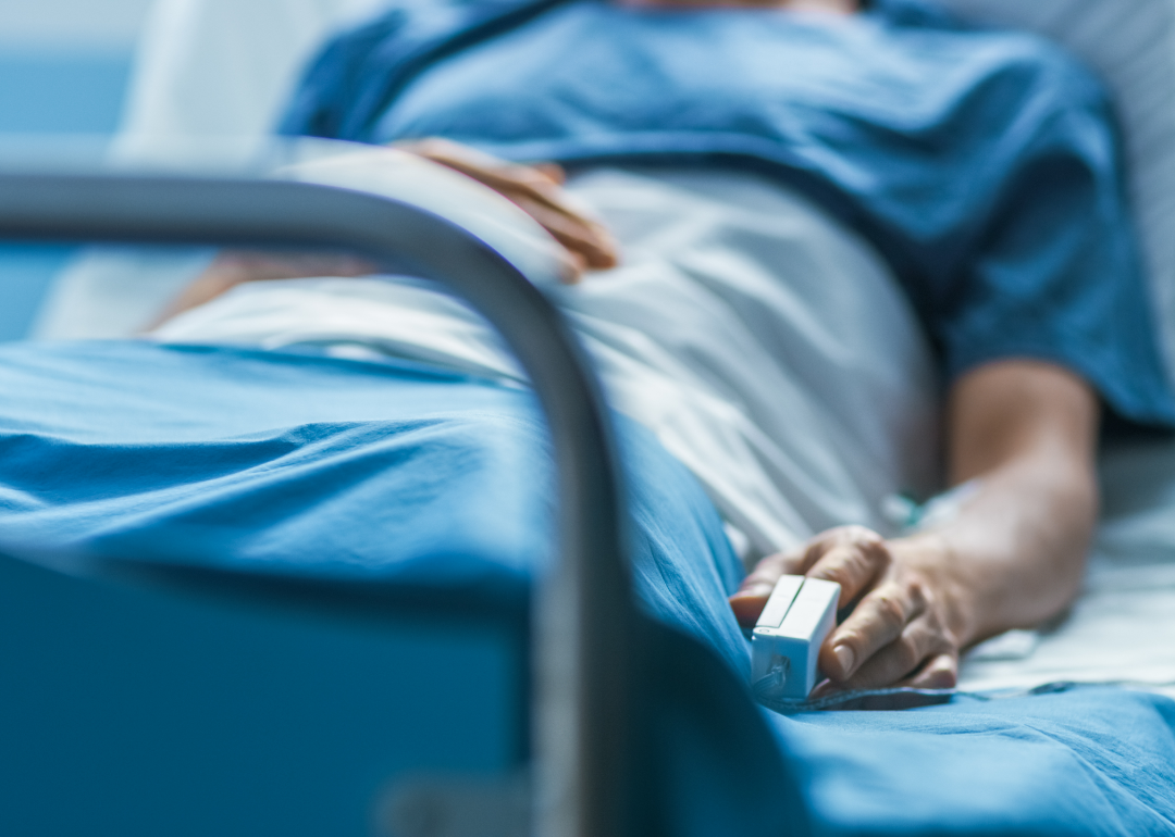 Person in hospital bed with pulse oximeter on their finger.