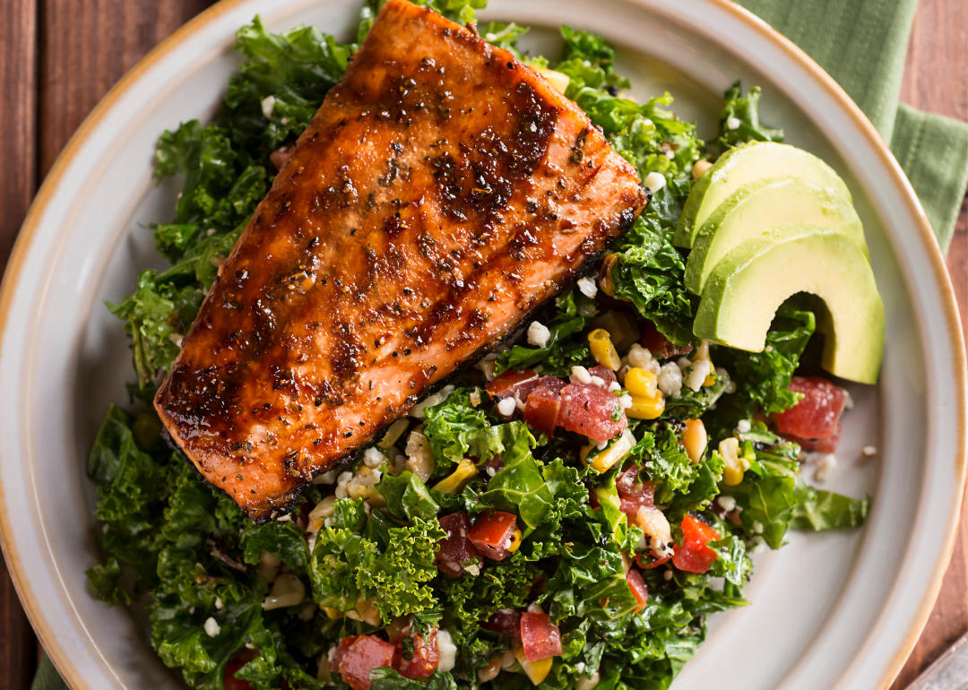 Grilled salmon with a kale salad and avocado on a white plate.