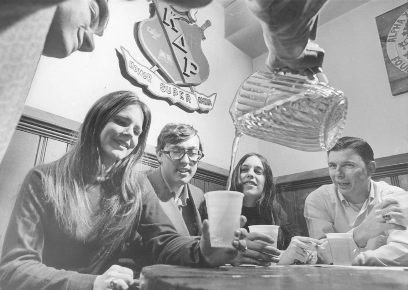 College students sitting at a table enjoying a pitcher of beer.