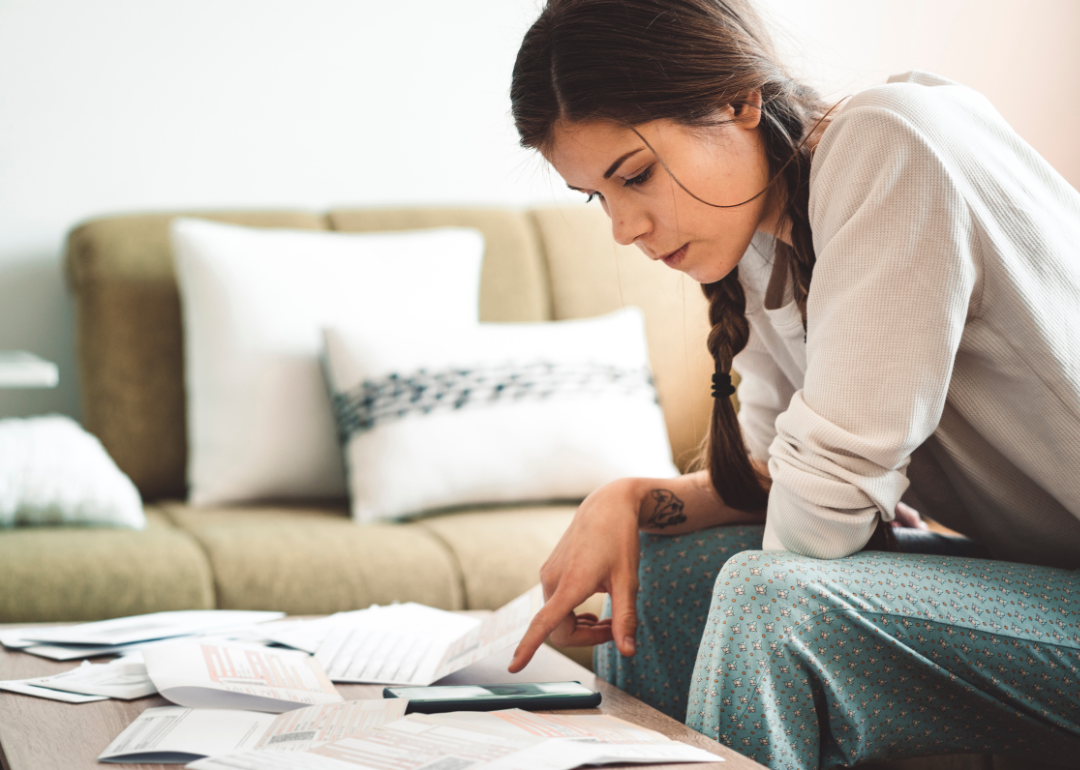 Young person sits in living room looking over bills.