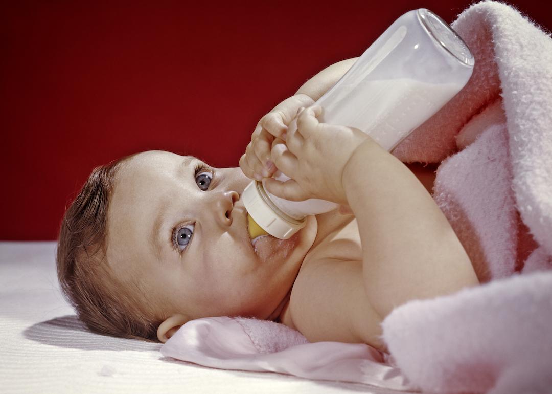 Baby in the 1960s holding a bottle while wrapped in a pink blanket.