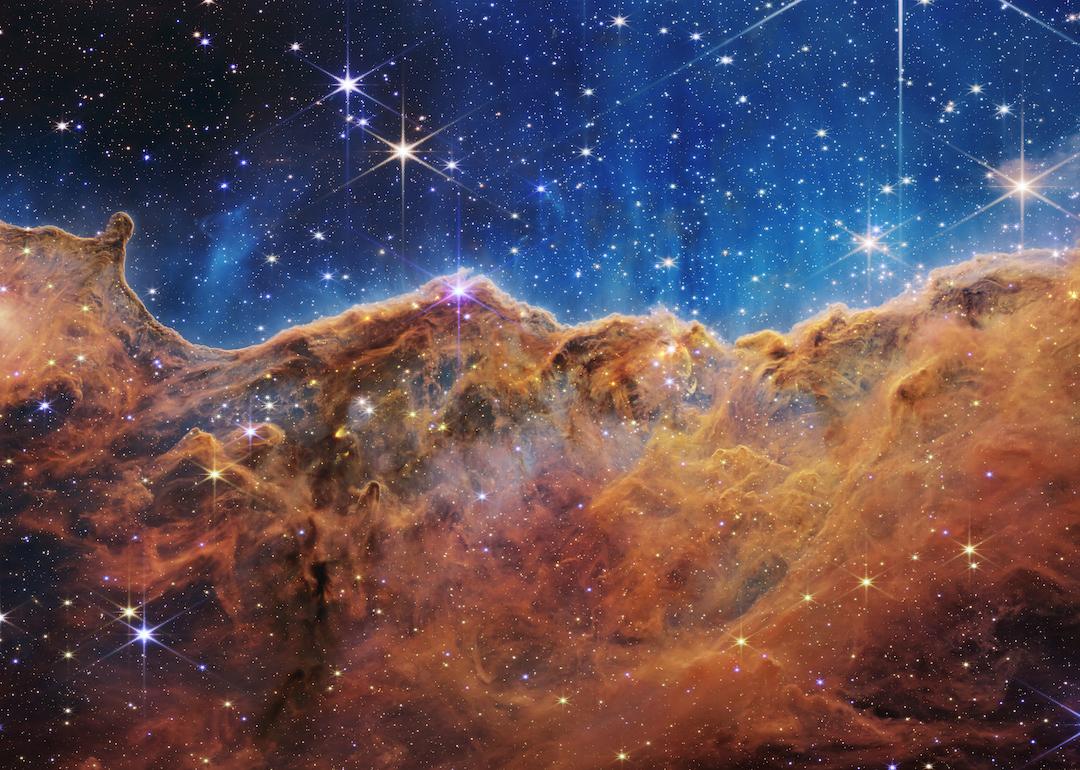 A landscape of mountains and valleys speckled with glittering stars is actually the edge of a nearby, young, star-forming region called NGC 3324 in the Carina Nebula, on July 12, 2022 in space. Captured in infrared light by NASA's new James Webb Space Telescope, this image reveals for the first time previously invisible areas of star birth. 