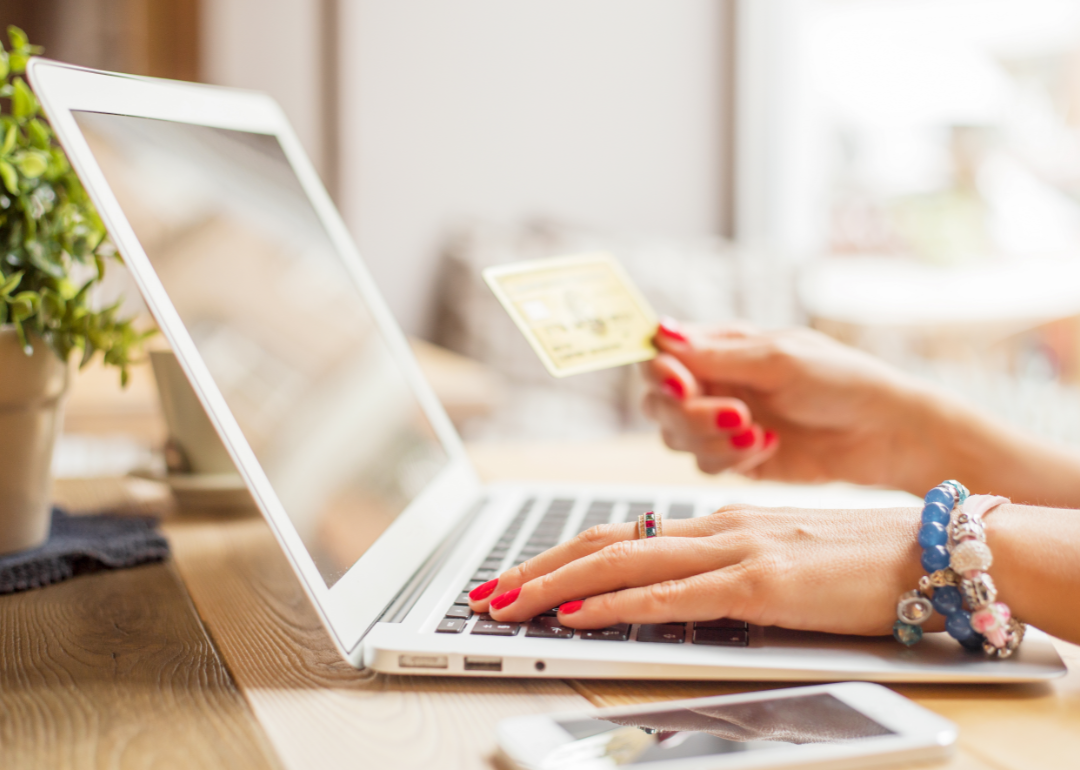 A person's hand on a laptop keyboard and holding a credit card.