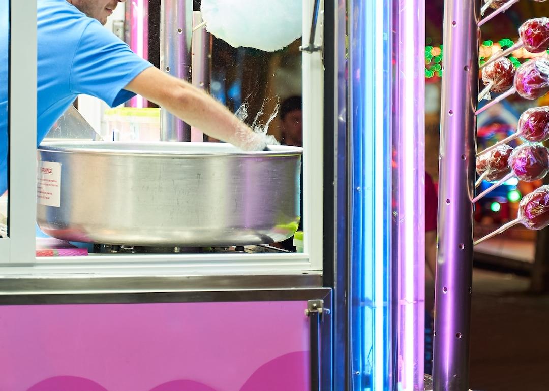 Young person making cotton candy at an amusement park booth.
