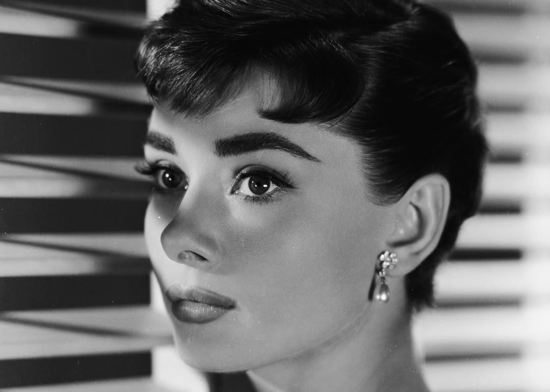 Actor Audrey Hepburn stares out window in black and white photo.