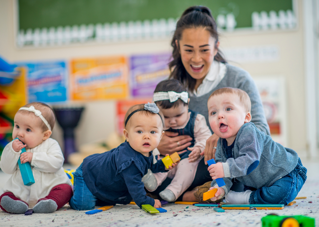 Infants and a caretaker sitting on a rug in a daycare facility