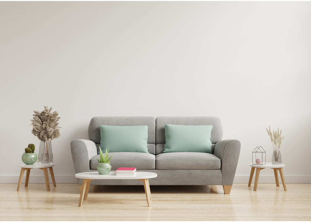 A gray sofa with green pillows with small wood end tables and coffee table