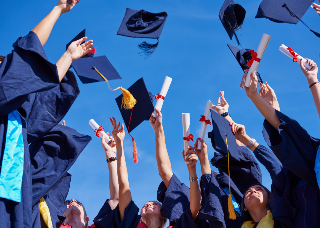 Students at a high school graduation holding diplomas and throwing graduation caps 