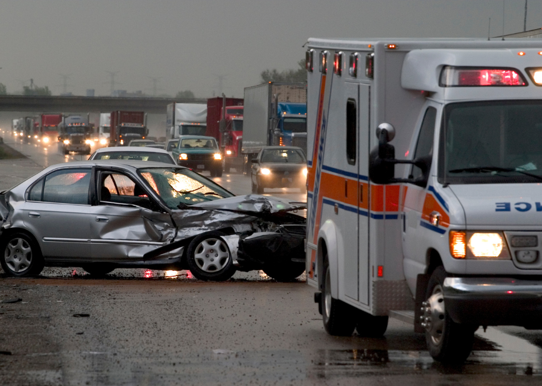 An ambulance pulls up to the scene of a traffic collision where a silver sedan has been totaled