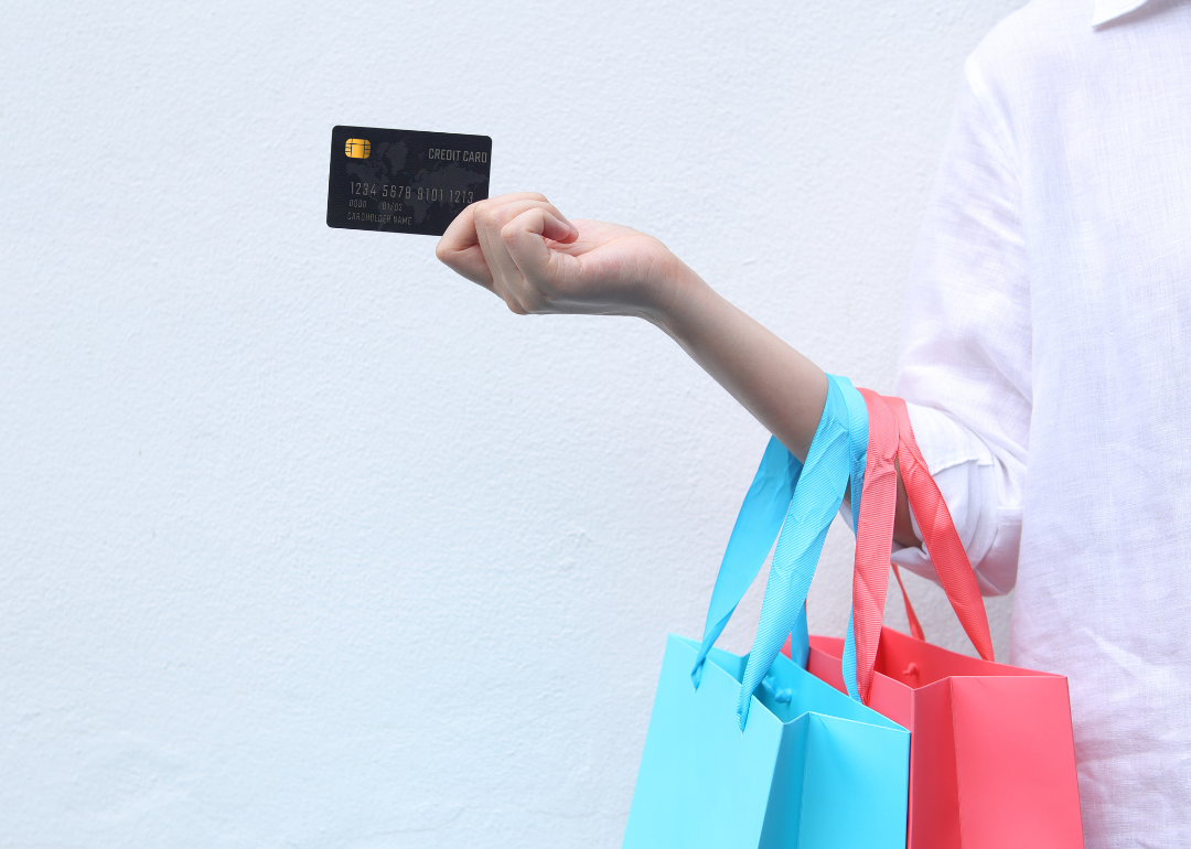 A woman holding a credit card and multi-colored shopping bags against a white background