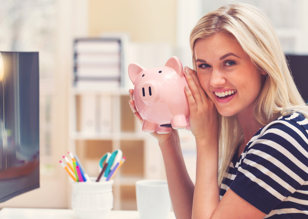 A young blonde woman in a striped shirt smiling an holding a piggy bank