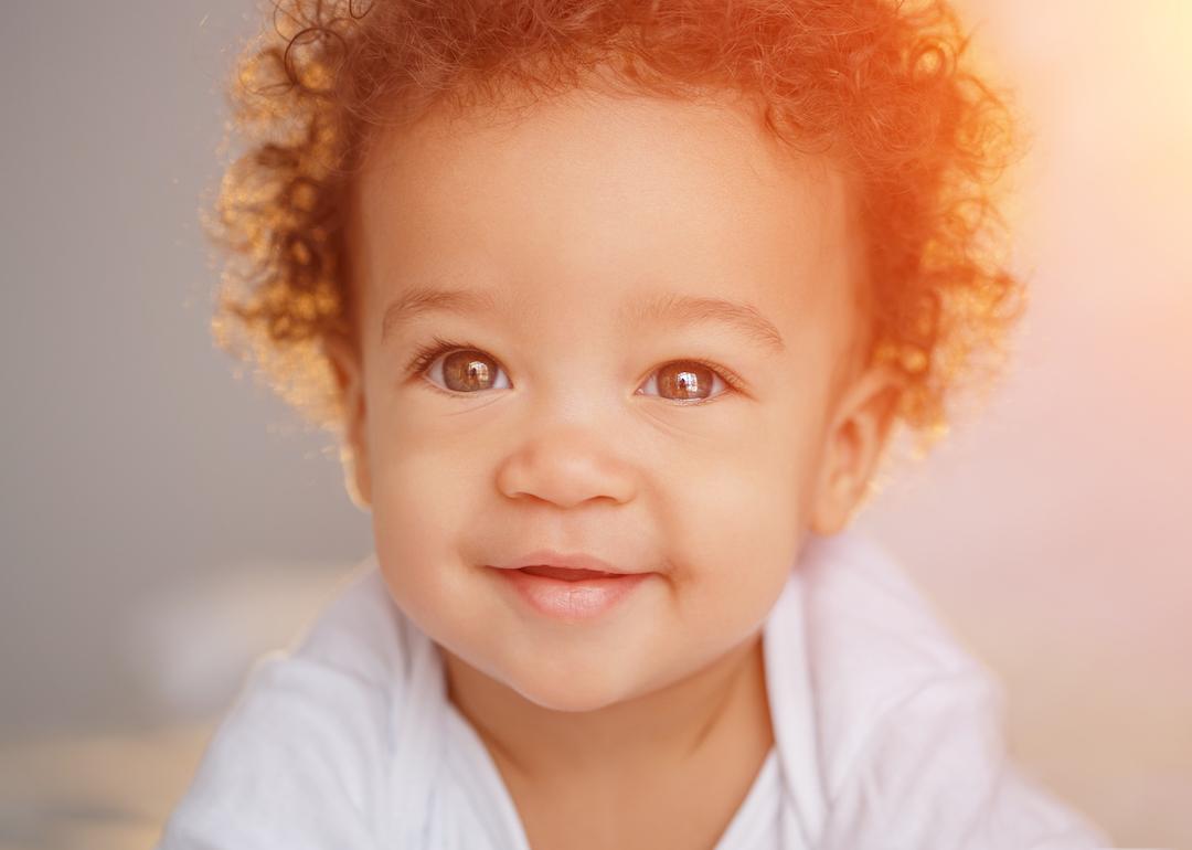 Smiling baby with curly hair in a white shirt.