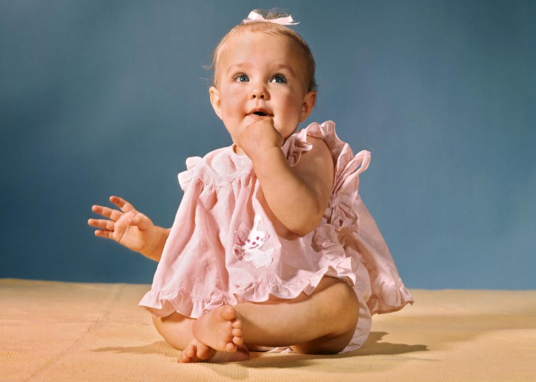 Baby in pink dress with white ribbon in the 1960s.