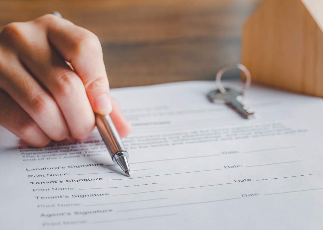 A rental agreement form that a landlord is resting a pen against to show details to a presumed tenant