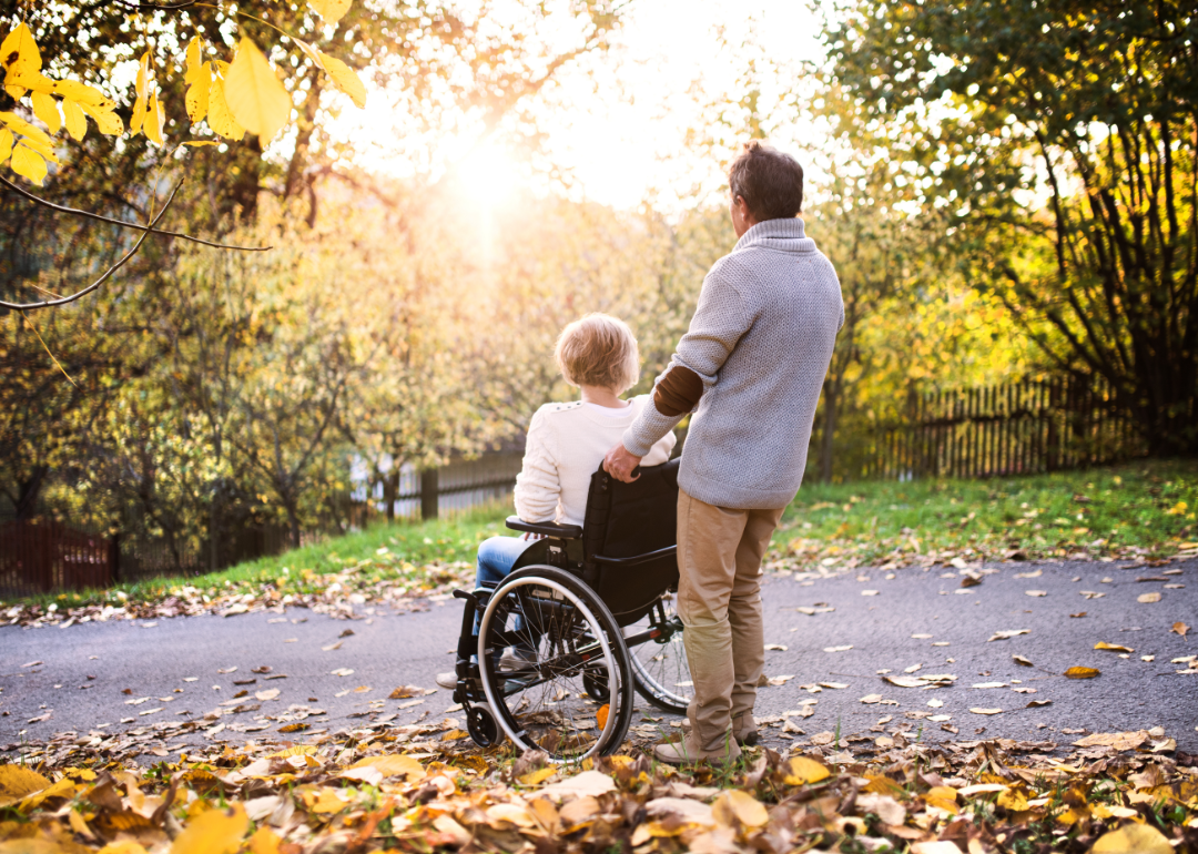 Senior couple, one of them in a wheelchair, watching the sunset amidst autumn foliage