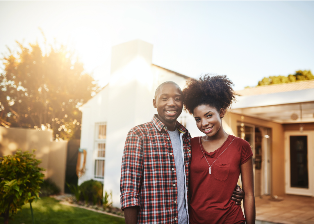 A young Black couple standing outside a home