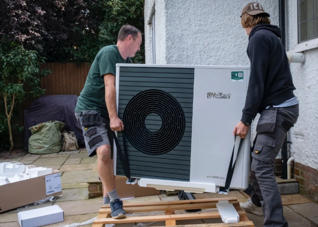 Two men installing a heat pump at a residential home