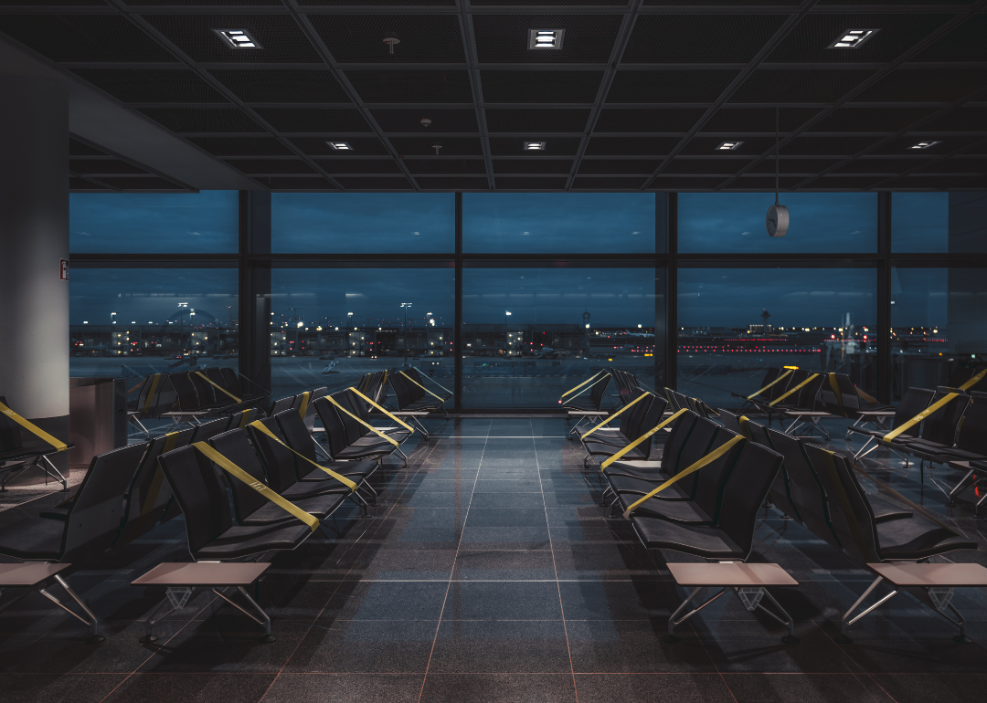 A wide-angle view of a dark empty abandoned quarantined waiting hall of a modern airport terminal at night, on a lockdown with regular greenish tapes over the seats to maintain social distancing