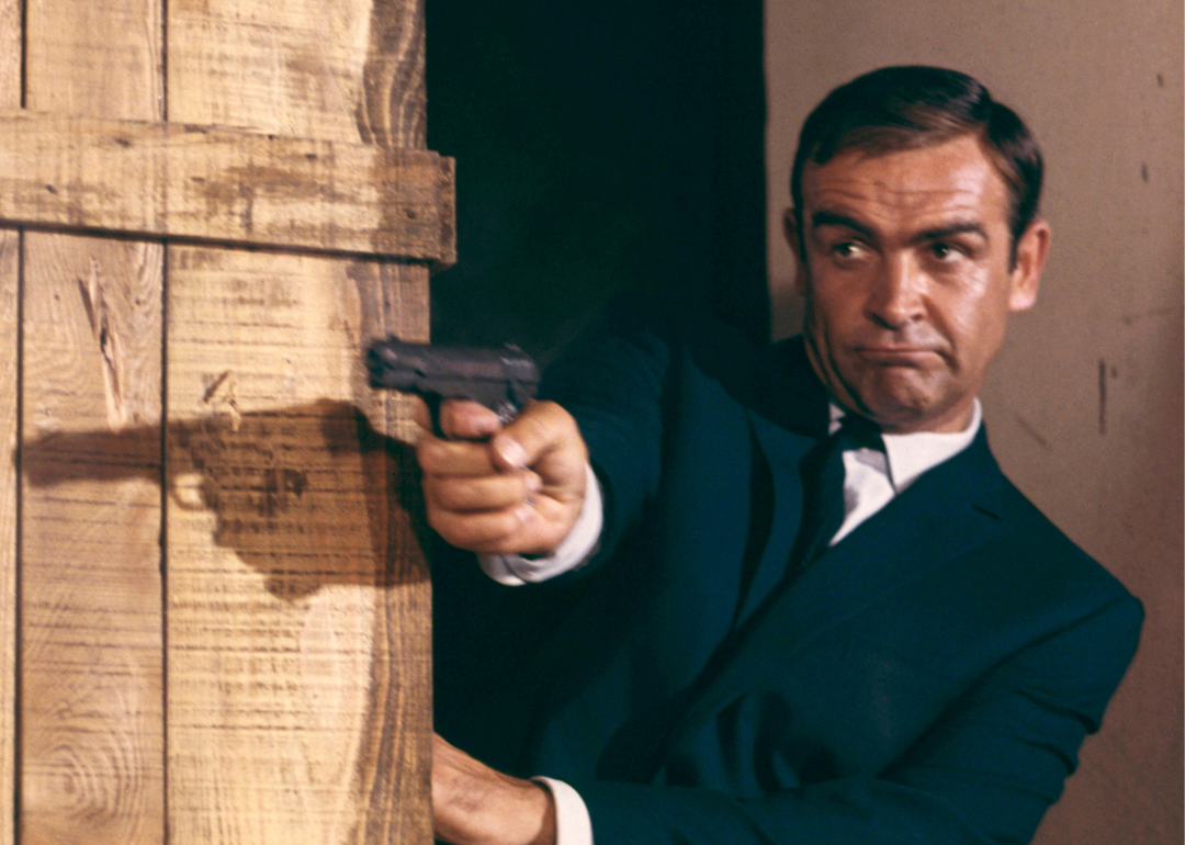 Sean Connery as James Bond firing pistol behind crates in a scene from "Goldfinger", 1964.