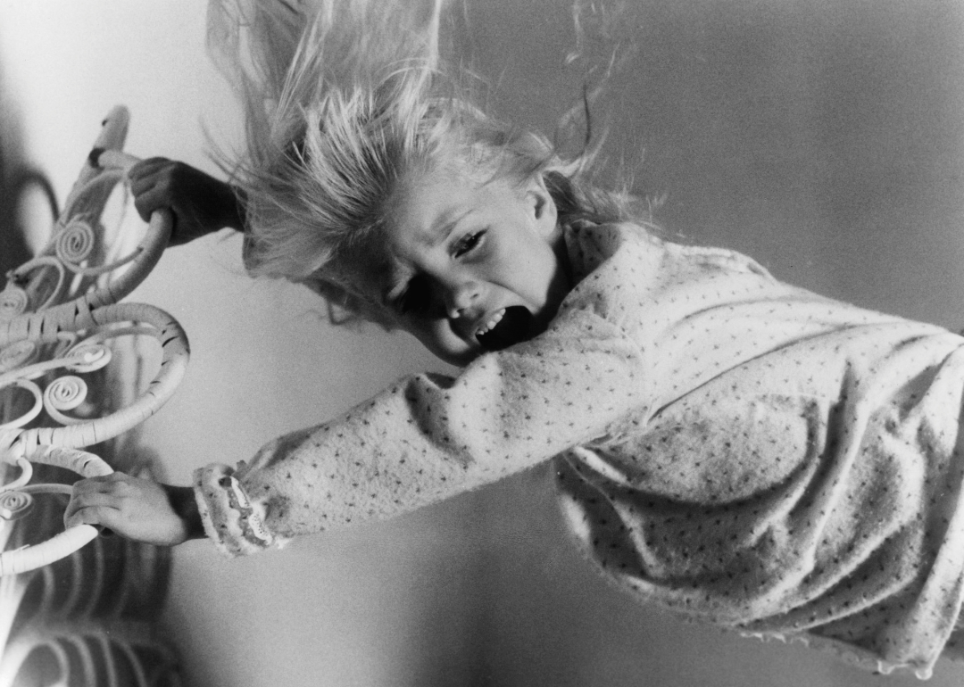 A young Heather O'Rourke holding on to a metal bedframe as she is attempted to be captured by evil spirits in a scene from the film 'Poltergeist', 1982.