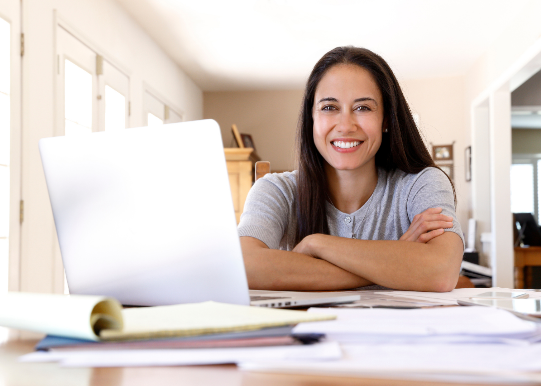 A smiling Latina woman sitting at a desk, near a laptop
