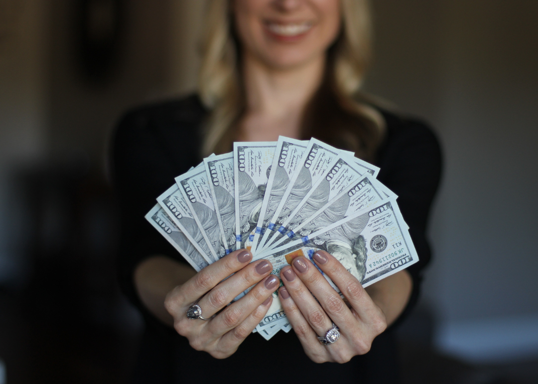 A woman holds up a fan of $100 bills