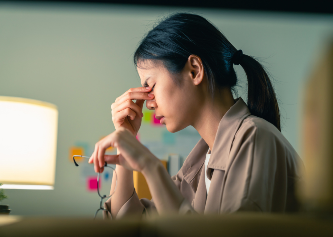 A young Asian American woman pinches the bridge of her nose in a posture of stress