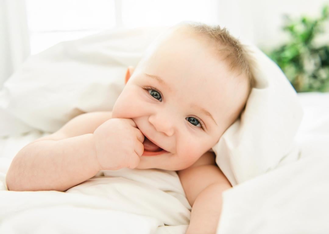 Smiling baby with blue eyes wrapped in a white blanket.