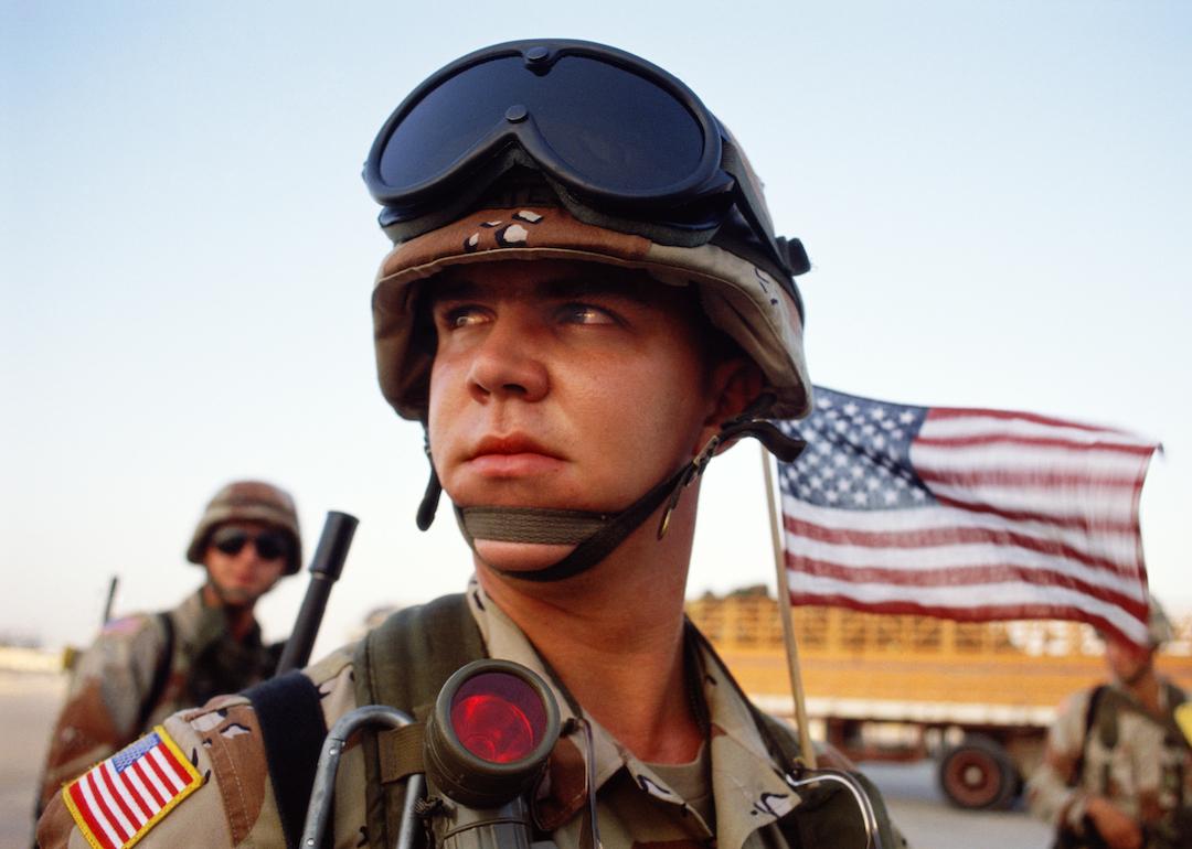 A young U.S. marine arrives at Dhahran Air Base with the American flag flying behind him, during the Gulf War, in December 1990.