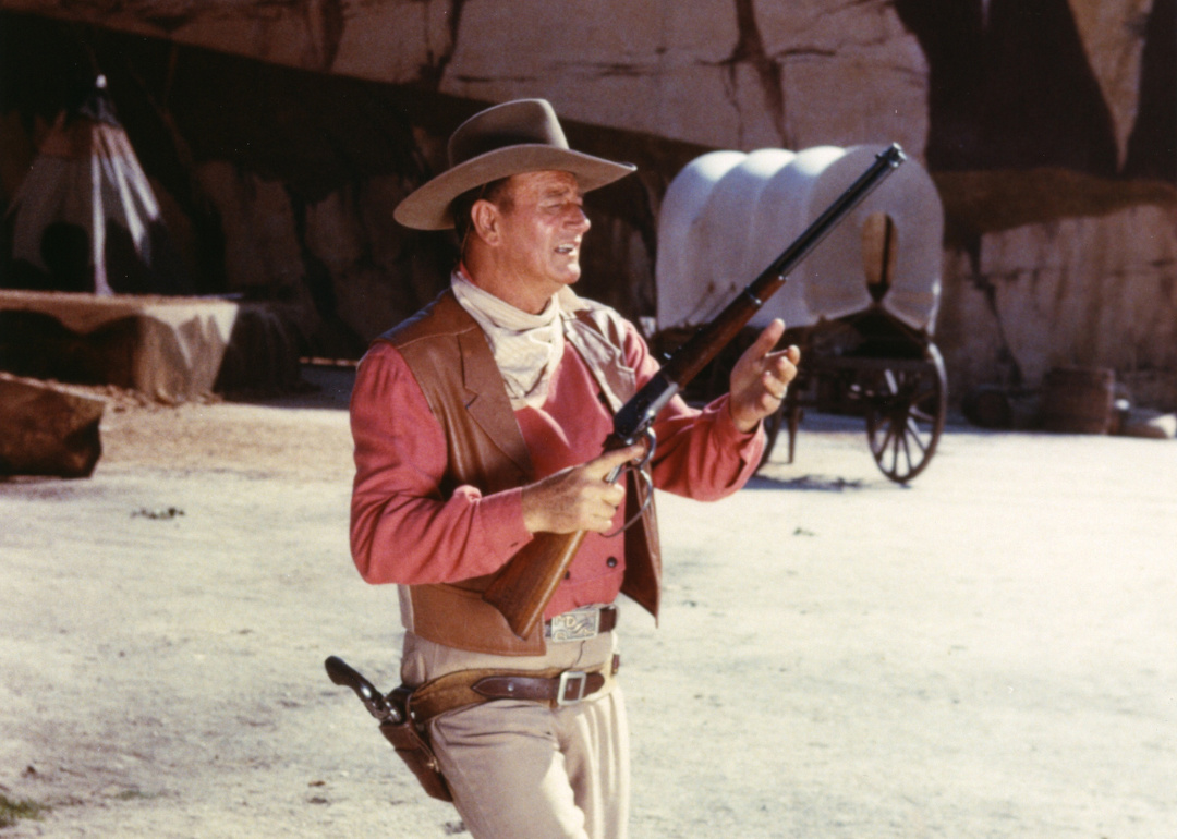 John Wayne, wearing a tan leather waistcoat over a pink shirt, taking aim with a rifle, in a publicity still issued for the film, 'Rio Bravo', 1959. 