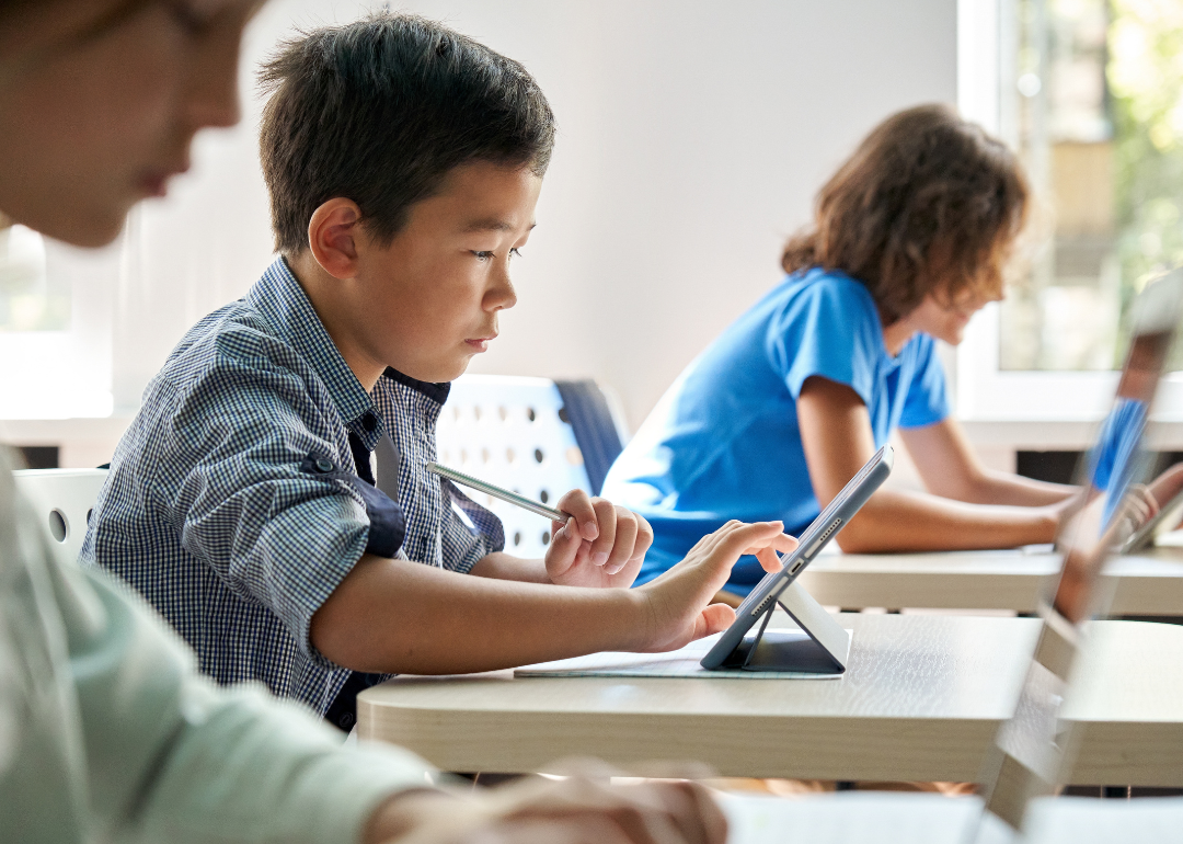 Focused Asian school boy using digital tablet at class in classroom.