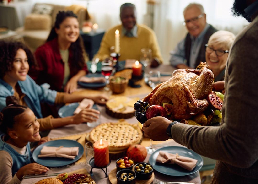Person serving turkey to their extended family during a Thanksgiving meal.