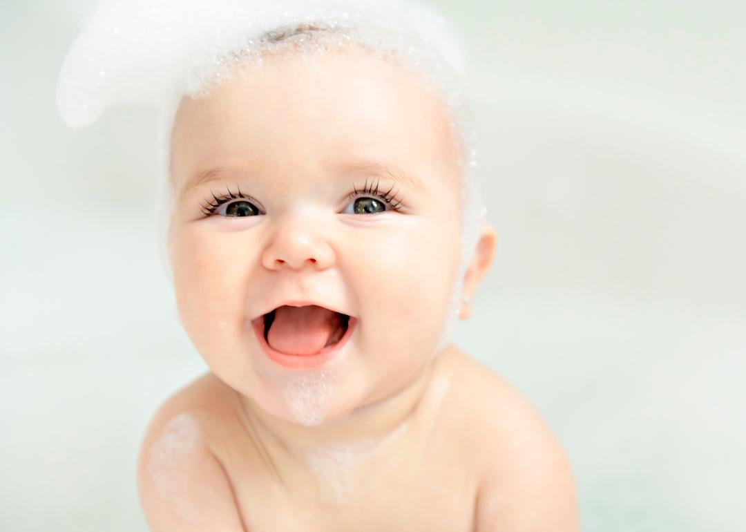Baby smiling with big blue eyes and bubbles on their head.