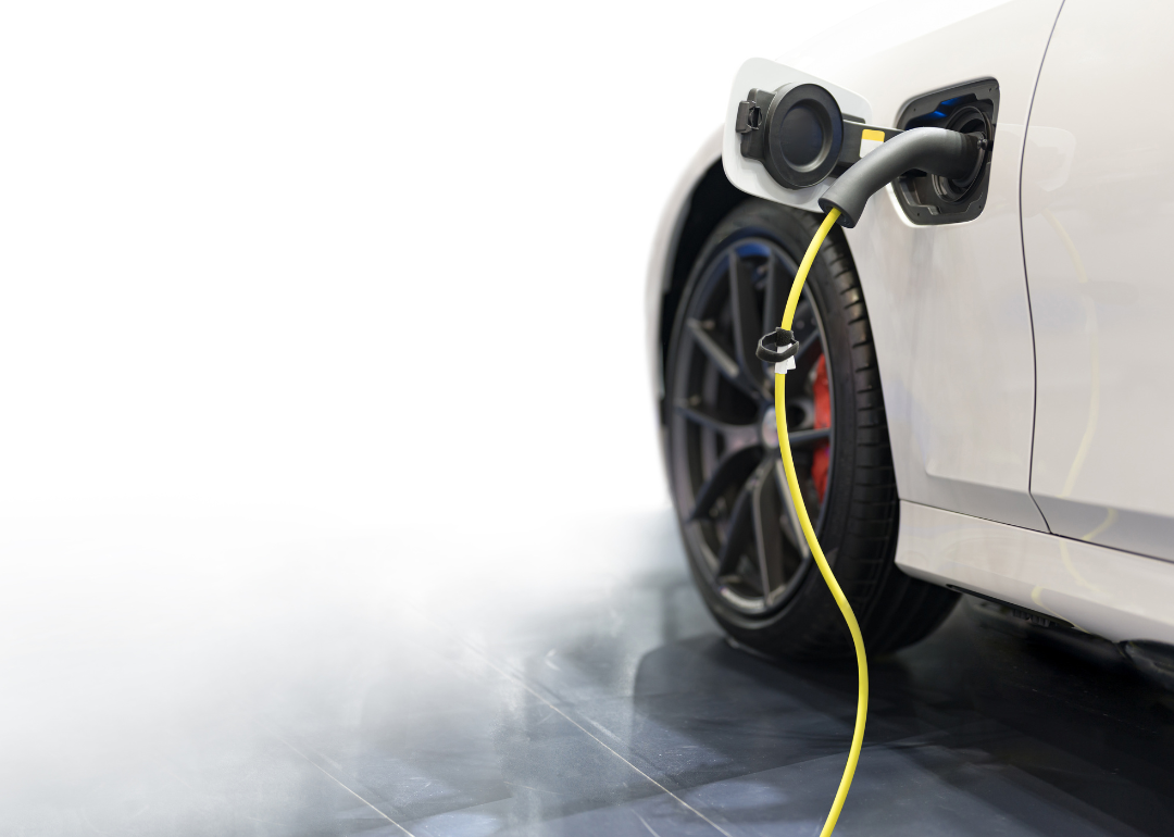 An electric vehicle plugged in to charge with smoke in the background to signify a possible battery fire