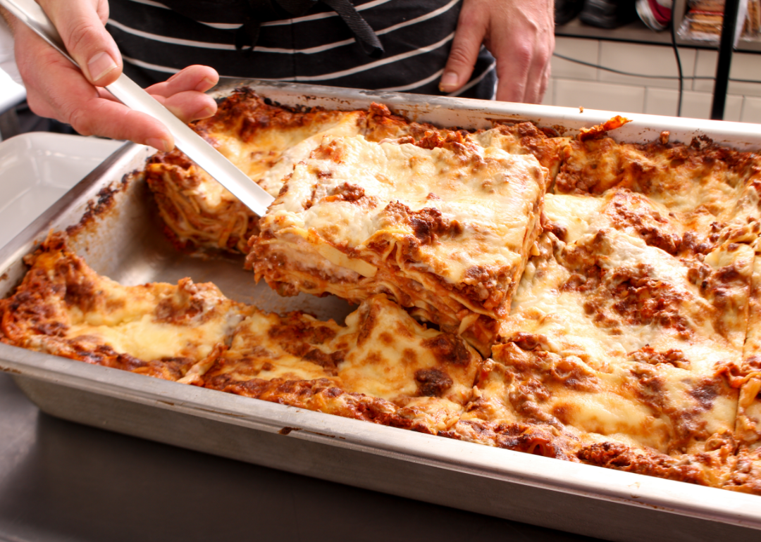 Person's hands cutting out a slice of lasagne from a baking pan