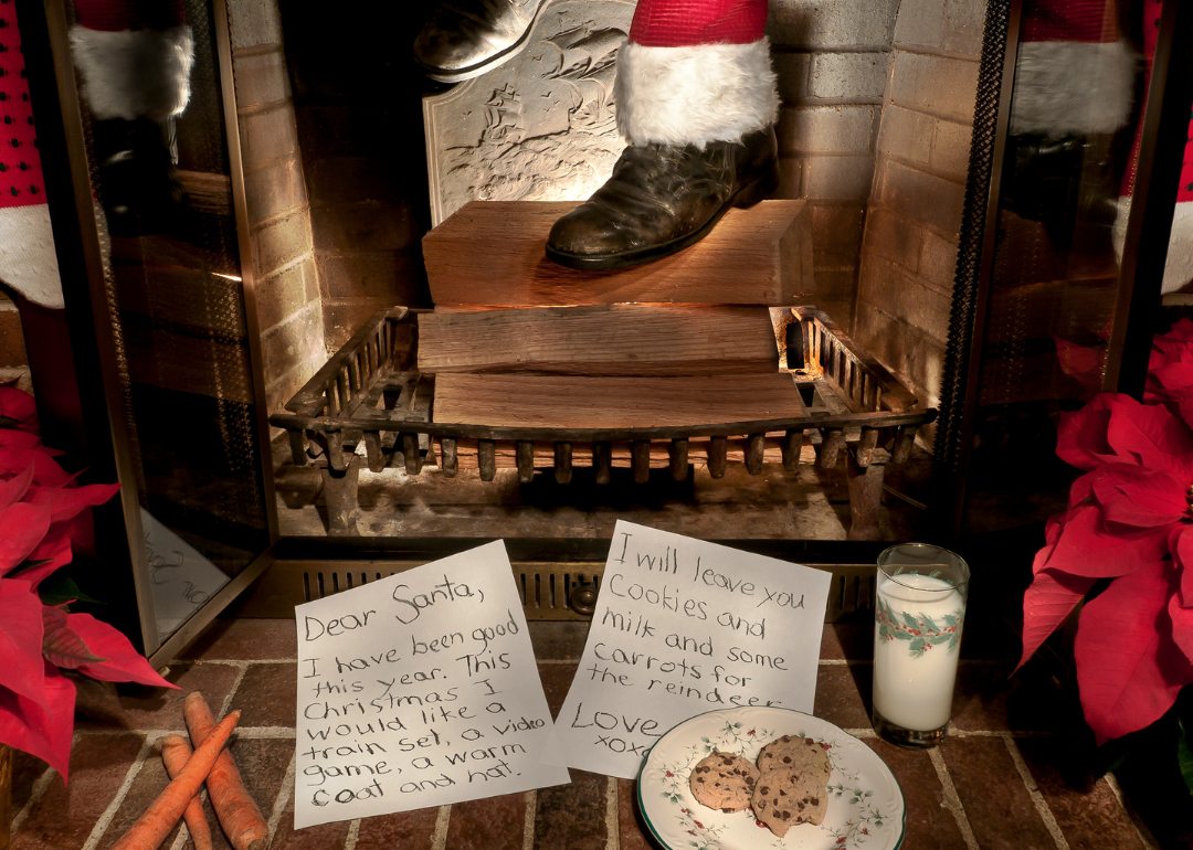 Santa's feet emerging from a chimney with a letter to Santa and cookies in the foreground