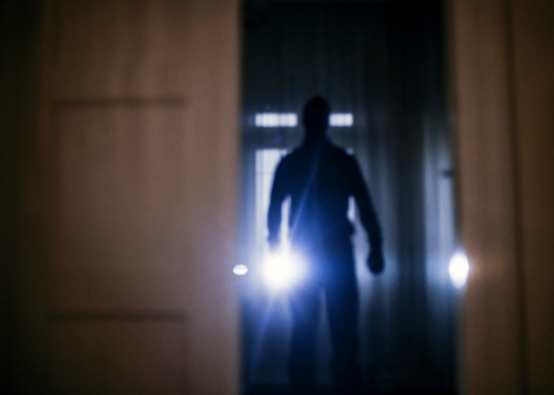 A blurred image of a burglar with a flashlight entering a home 