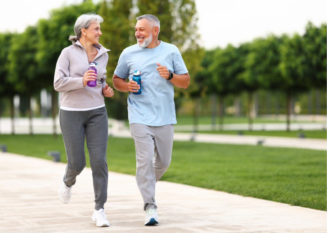 Senior couple smiling at each other while jogging through a city park