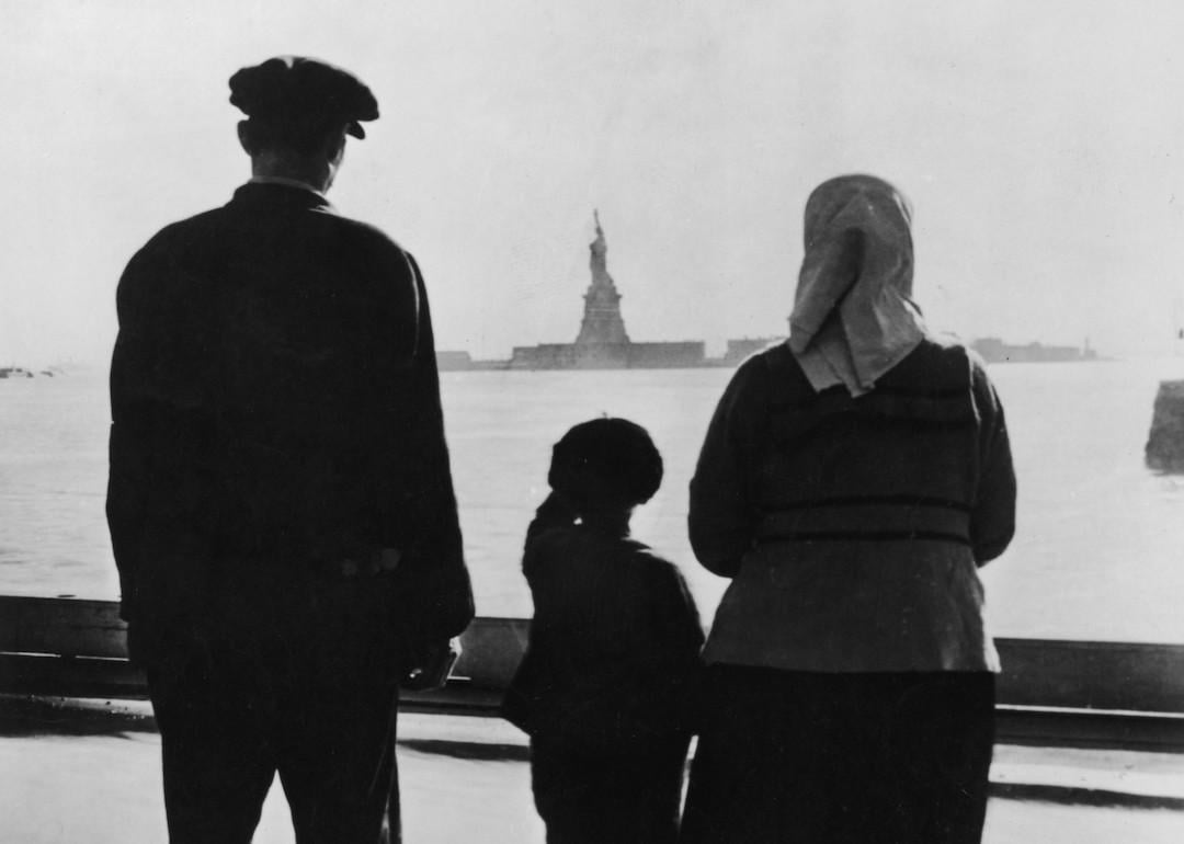 Rear view of an immigrant family on Ellis Island looking across New York Harbor at the Statue of Liberty in the 1930s.
