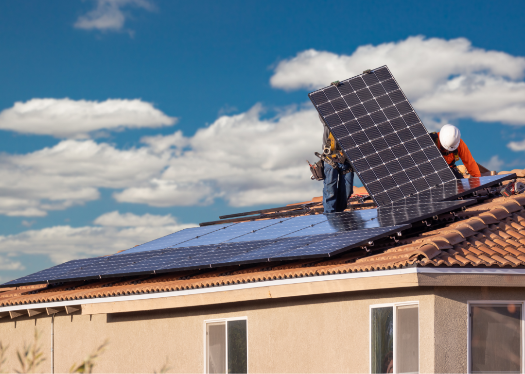 two workers installing solar panels on spanish tile roof house 