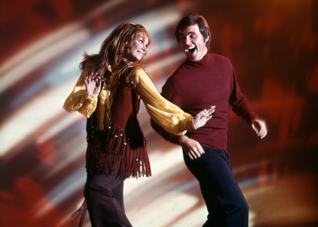 A couple dancing at a disco club in the 60s wearing typical outfits of the decade, bell bottoms and fringed vests 