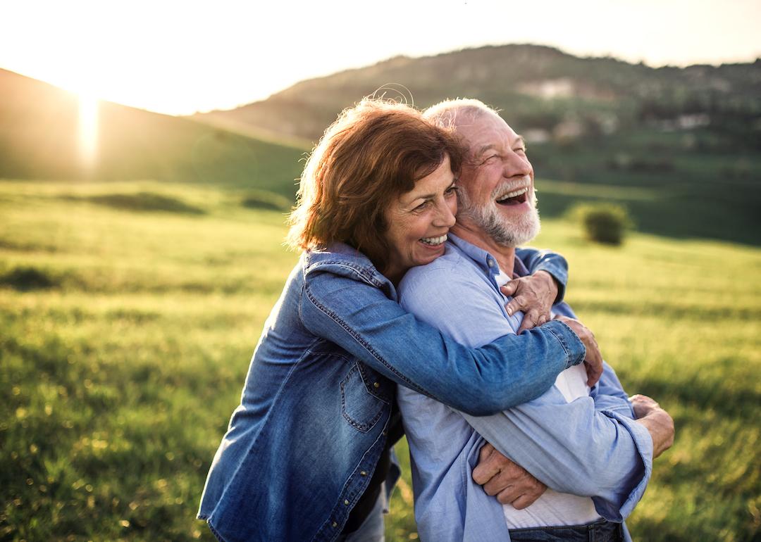 Side view of senior couple hugging outside in nature at sunset.