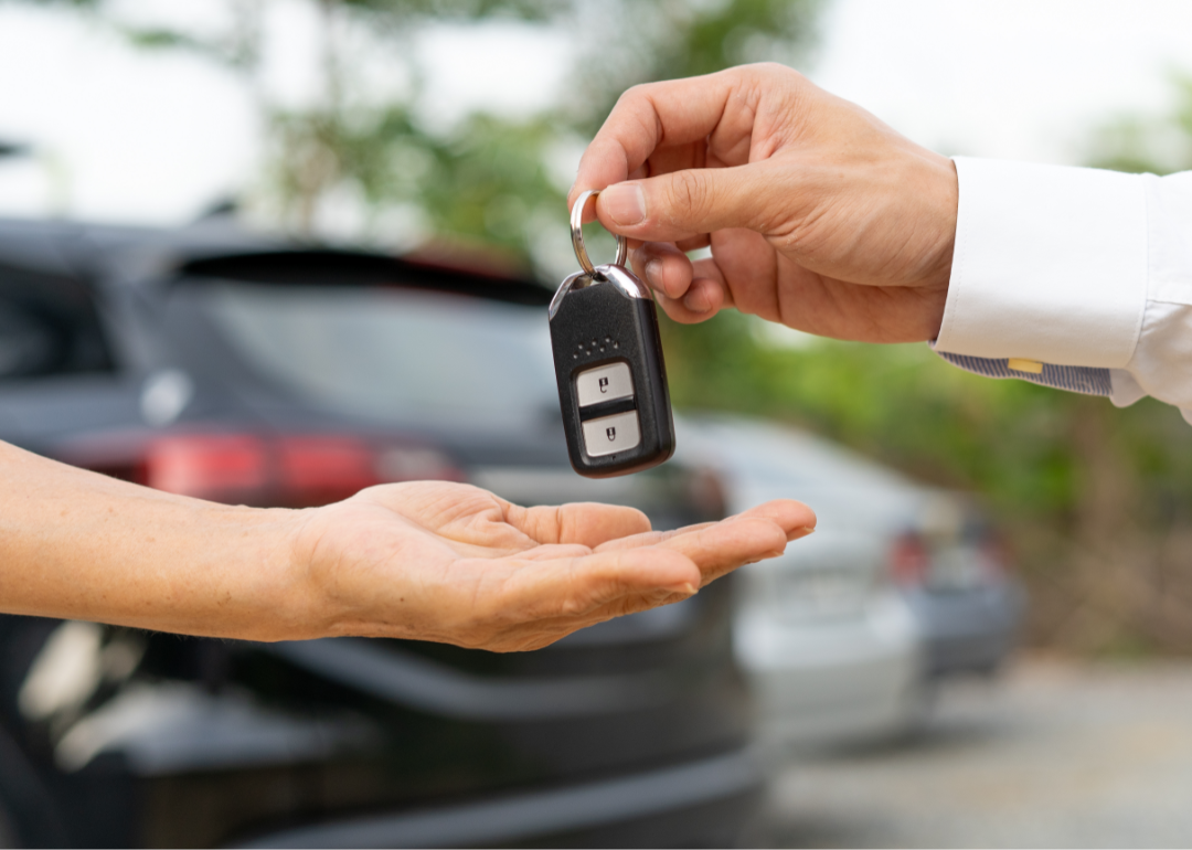 one person handing over car keys to another with cars in background