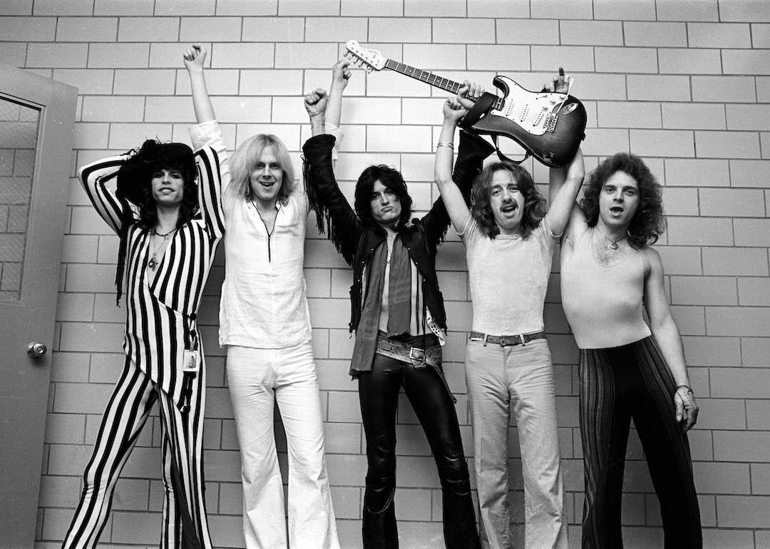 The members of Aerosmith— Steven Tyler, Tom Hamilton, Joe Perry, Brad Whitford, and Joey Kramer—pose backstage with a guitar in 1976.