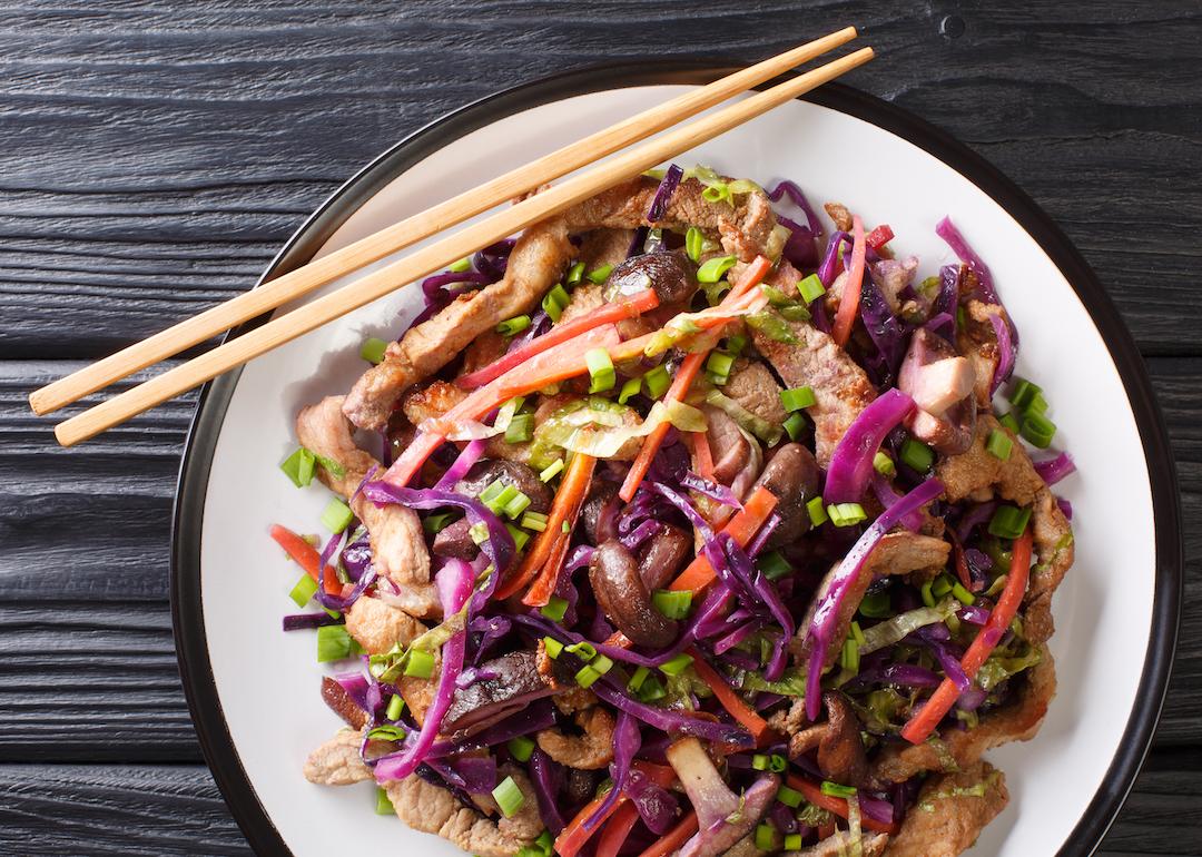 Moo shu chicken with cabbage and mushroom on a plate on a table with chopsticks.