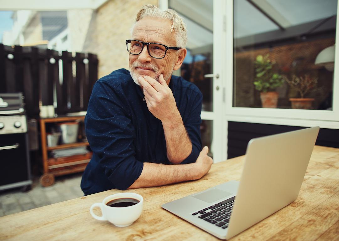 Retired person sits in their backyard drinking coffee in front of their laptop.